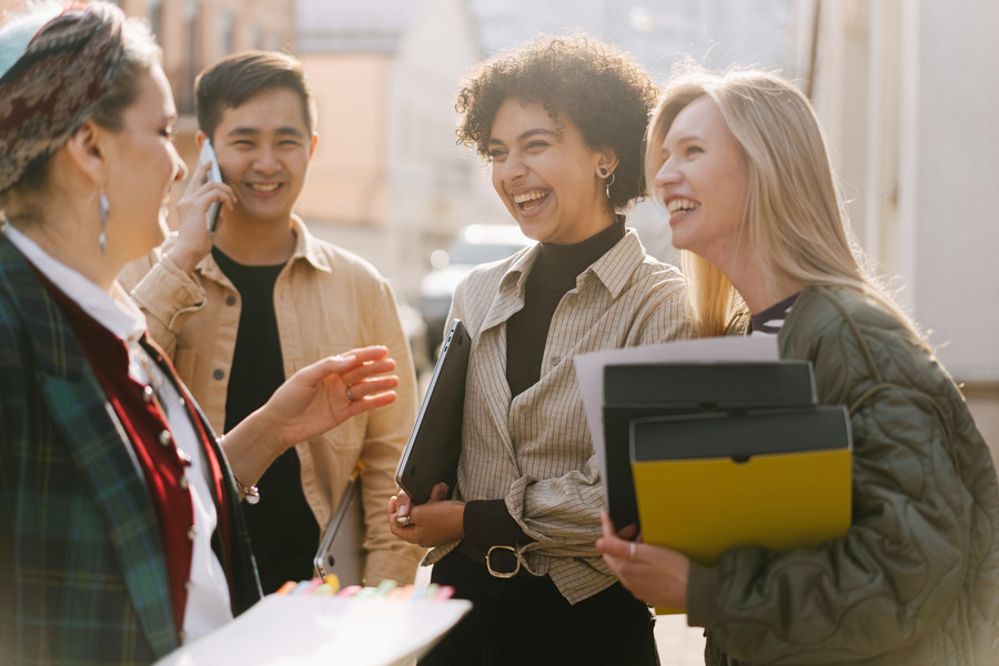 Group of smiling individuals talking outside on a sunny day.