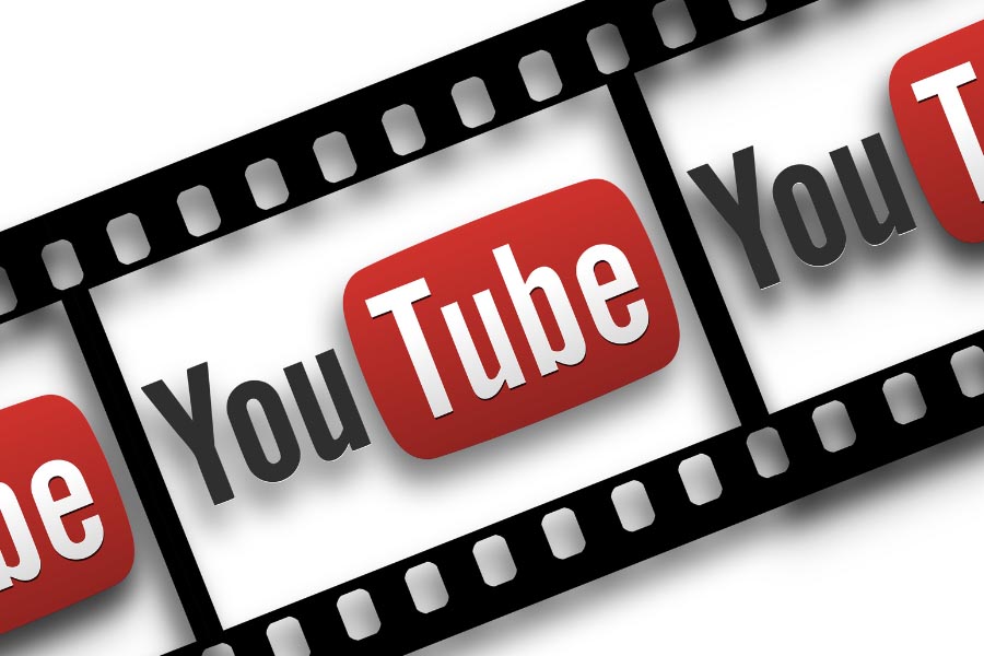 Black filmstrip running diagonally over white background, YouTube text and logo in photo area, credit – Canva.