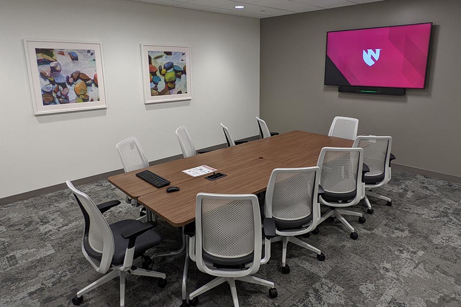 Chairs sit at four tables pushed together in the center of MMI’s small conference room, a flat screen TV on one wall, artwork on another.
