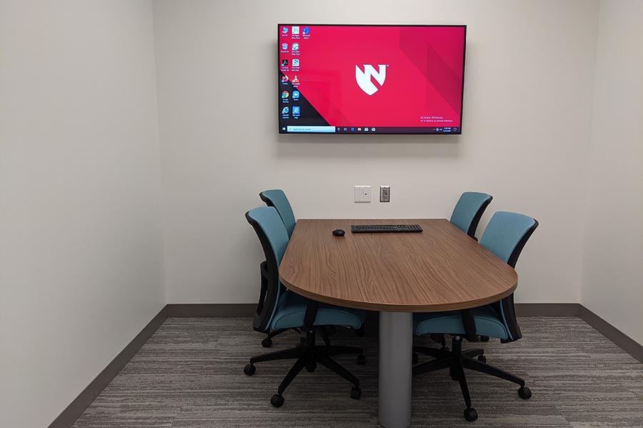 Four chairs sit at one oval table in an MMI community partner room, a flat screen TV on one wall.