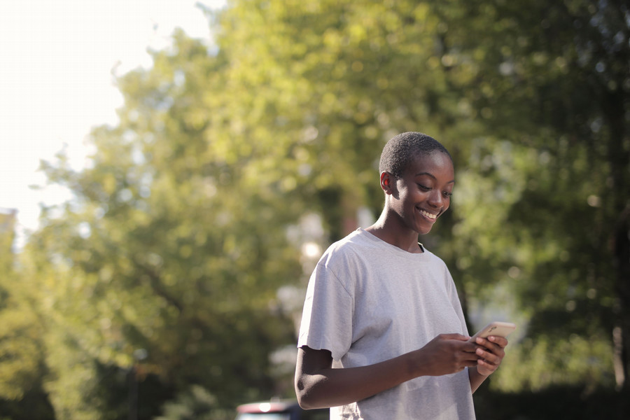 Young adult smiling down at their phone in a park.
