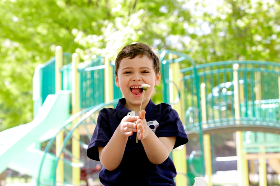 Smiling child holding a dandelion puff at a playground.