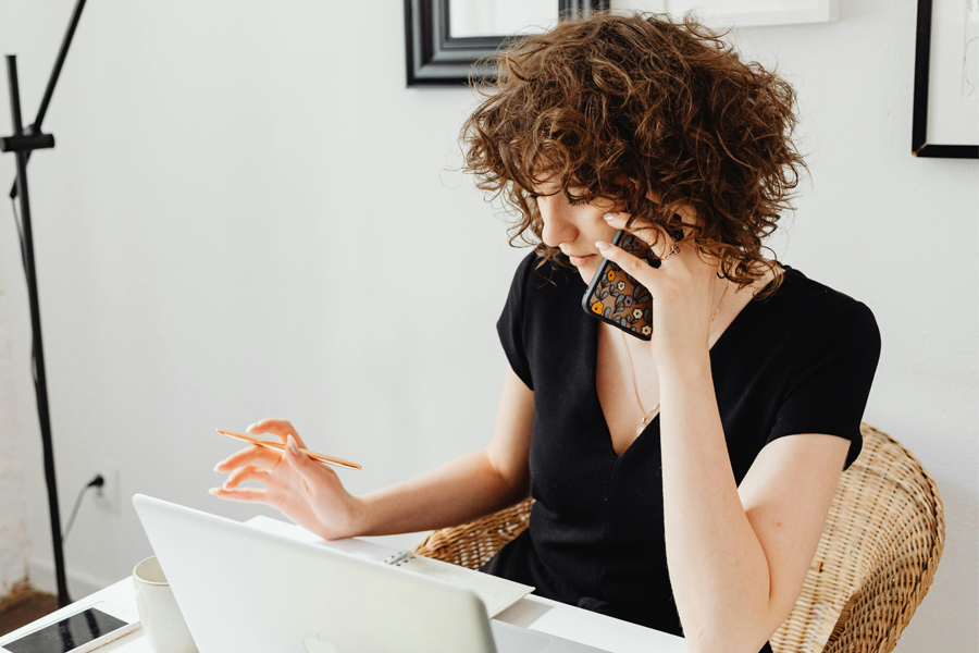 Young woman talks on the phone while working at her laptop.