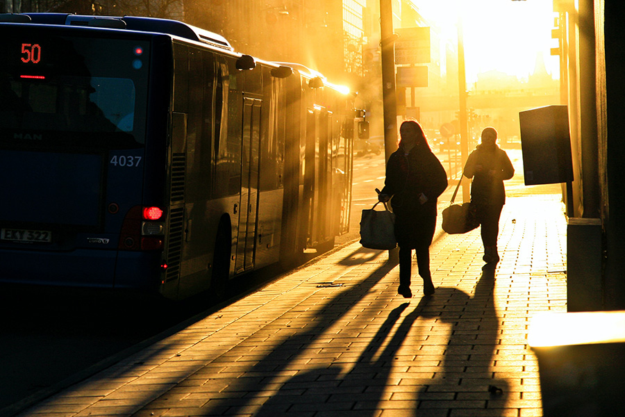 Two people walking next to a bus parked next to the curb on a street