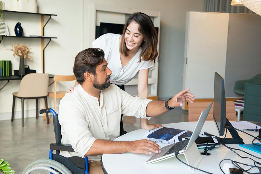 Person in wheelchair shows computer info to colleague.