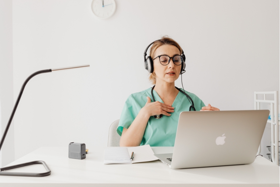 A medical professional with headphones on sits in front of a laptop.