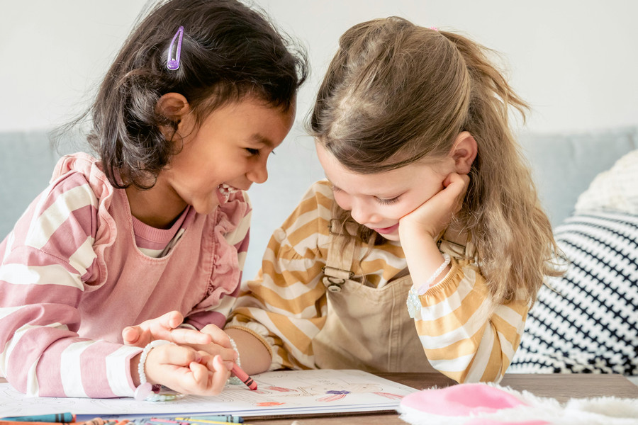 Two children sit at a table, coloring and laughing.