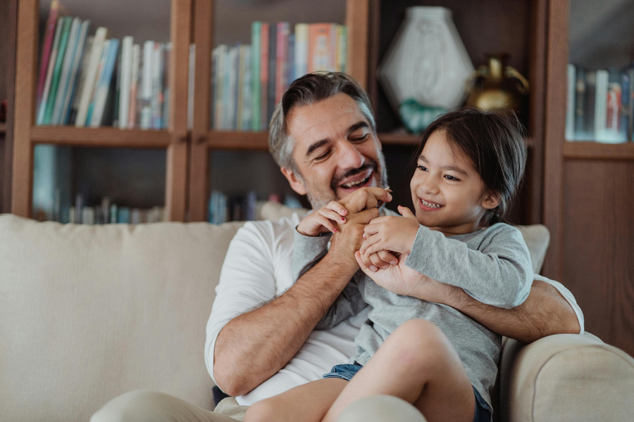 Parent hugging a laughing child, both seated on a couch.
