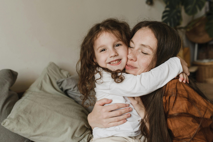 Child smiles at the camera and hugs parent around the neck.