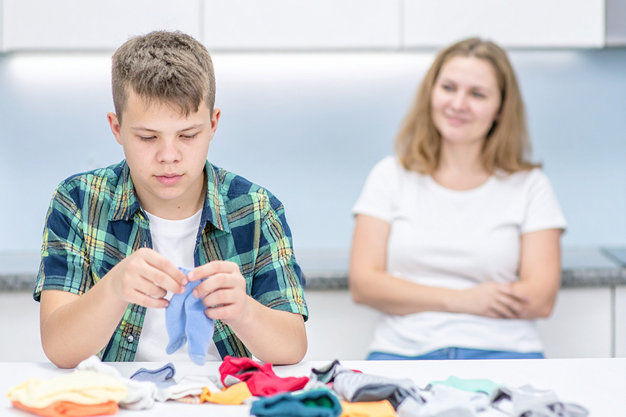 An AI-generated image of a young teen folding socks while a caregiver watches his progress.