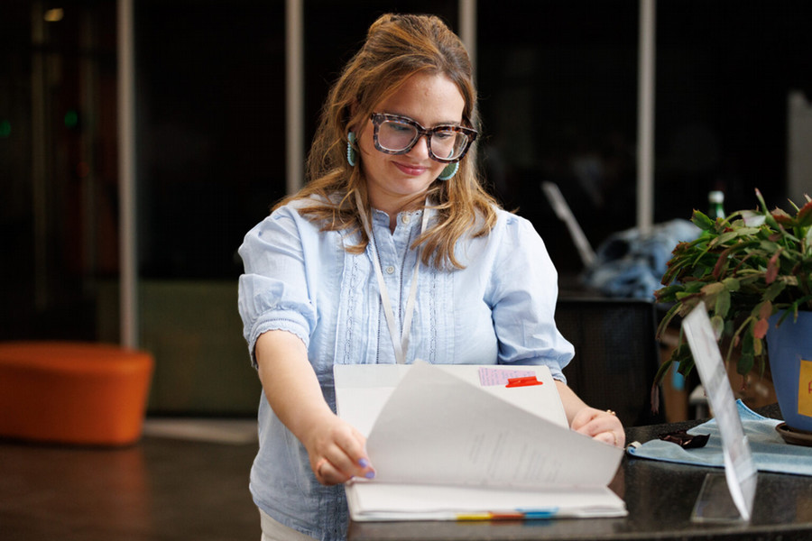 A woman in tortoiseshell glasses reads through a binder.