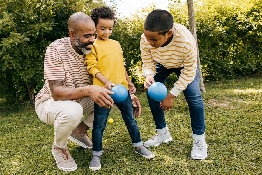 Caregiver playing ball outdoors with two children.