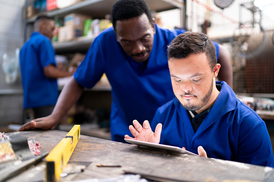 Two employed individuals focused on a task while using a handheld tablet, credit iStock.