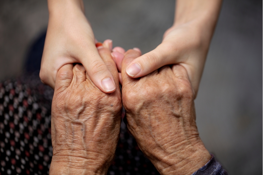 A pair of young adult hands holding the hands of an elder adult.