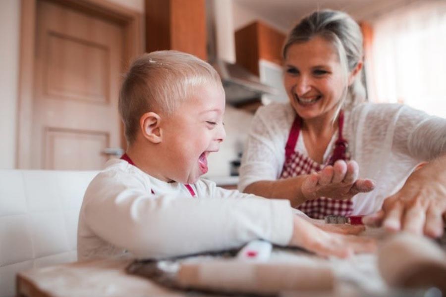 Caregiver and child in kitchen, baking together and laughing. 
