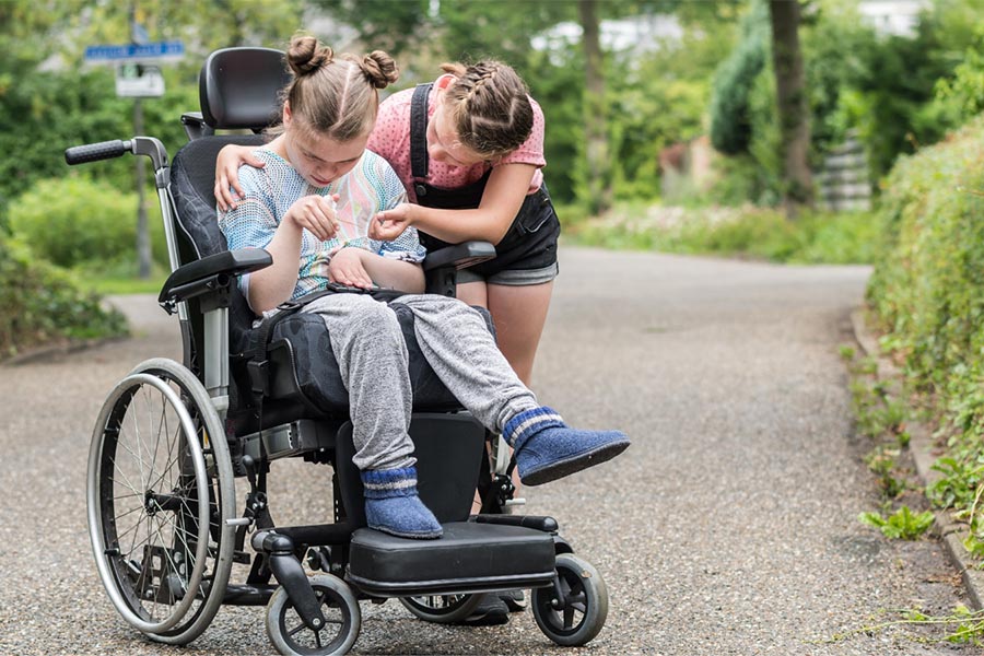 Adolescent wheelchair user with caregiver outdoors, Canva.