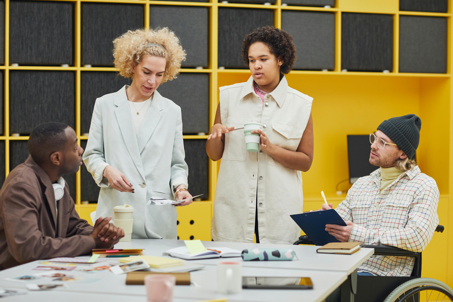 Four individuals have a meeting; one individual sits in a wheelchair.