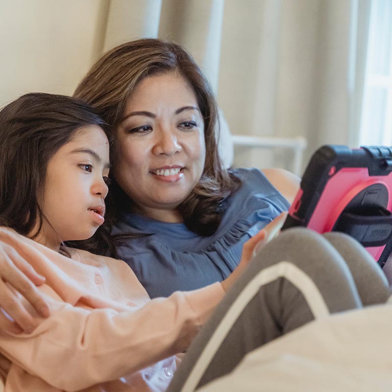 A woman helping a young girl use a tablet