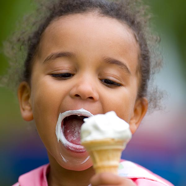 Child eating vanilla ice cream cone with ice cream around her mouth, iStock.