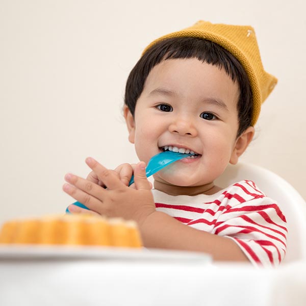 Child with fork in mouth sitting in feeding chair excited about dessert on tray, by Kazuend from Unsplash.
