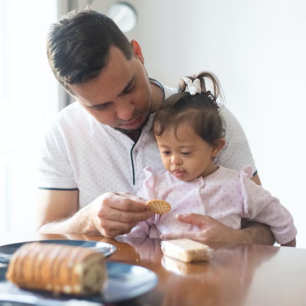 Father feeding daughter crackers at kitchen table, Kampus Production - Pexels.