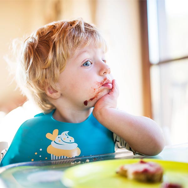 Child in feeding chair looking uninterested in food, from Canva.
