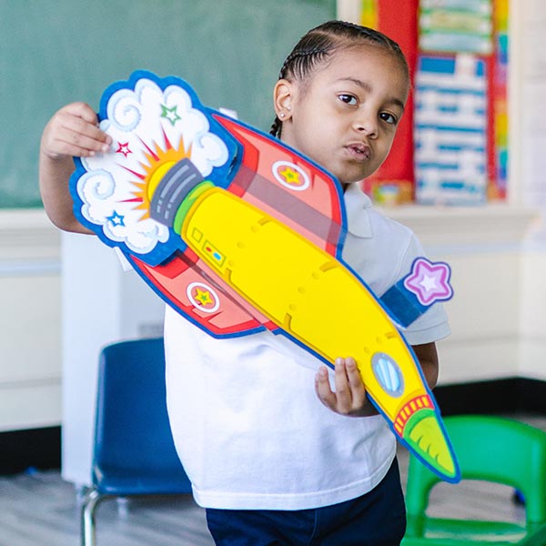 A young girl holding a colorful rocket ship made from paper