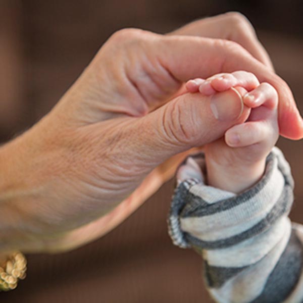 An adult hand carefully holding an infants hand