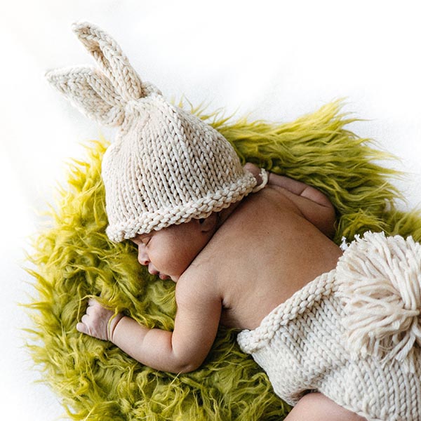 An sleeping infant wearing a knit bunny hat and diaper cover