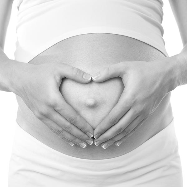 A woman holds her hands in the shape of a heart on top of her pregnant stomach