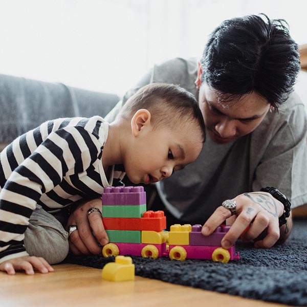 A father and son laying on the floor playing with a toy train