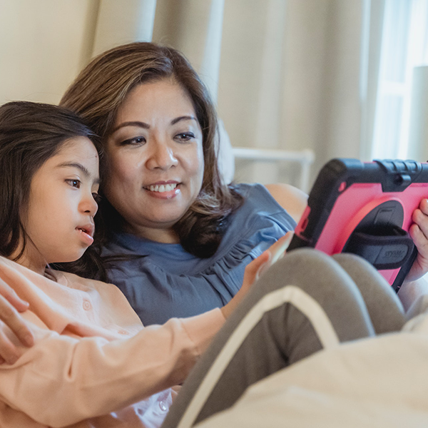 Child sitting with caregiver using tablet, by Nicola Barts – Pexels.