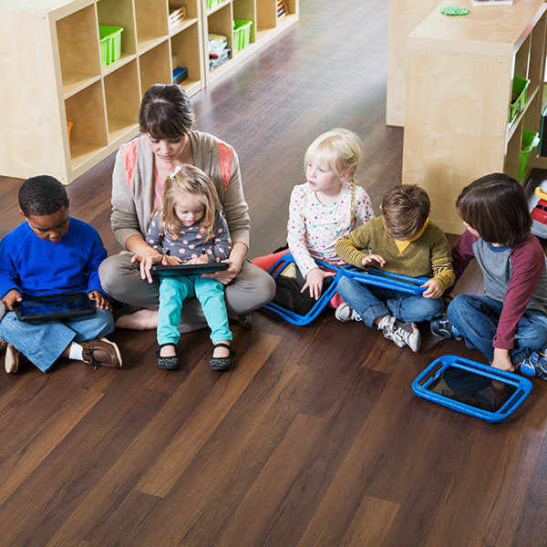 Children sitting cross-legged on floor with teacher, iStock.