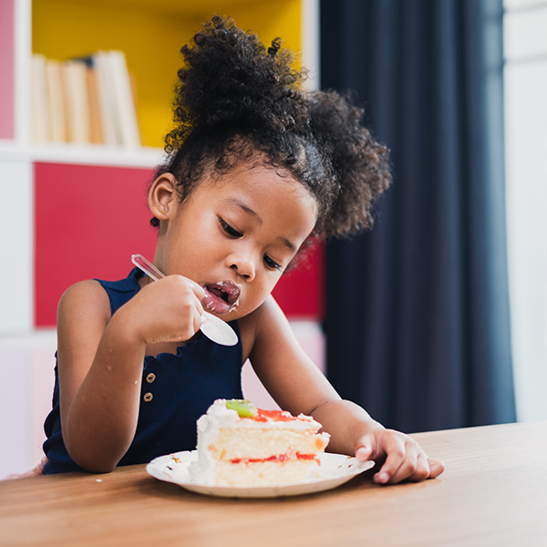 Girl holding spoon looking intently at cake, iStock.
