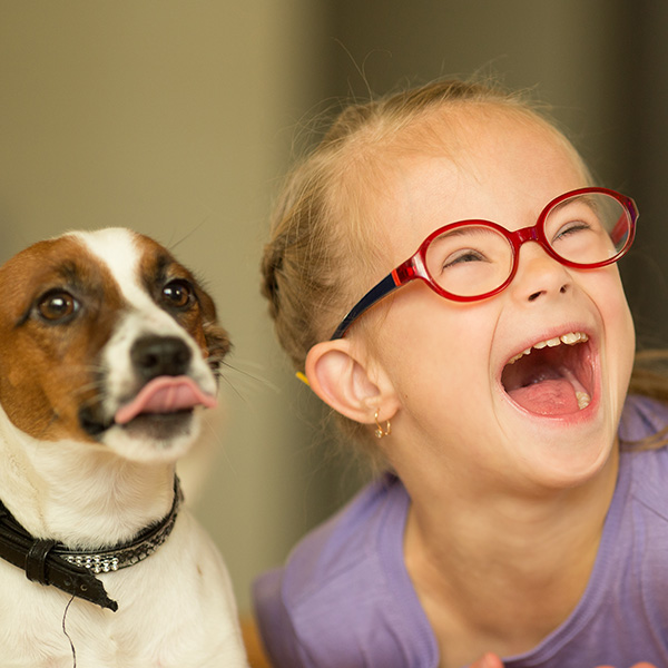 Girl wearing red glasses laughing next to dog sticking out tongue, Shutterstock.