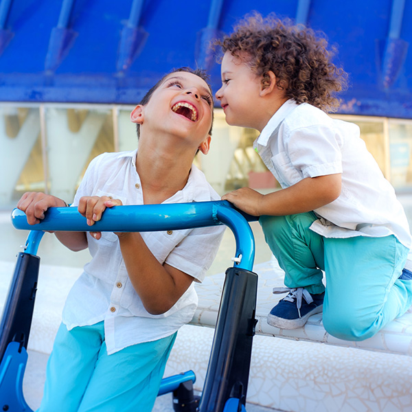 Adolescent boy using mobility device laughing with younger sibling, iStock.