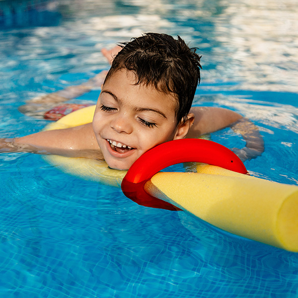 Child smiling in a pool with floatation noodles, iStock