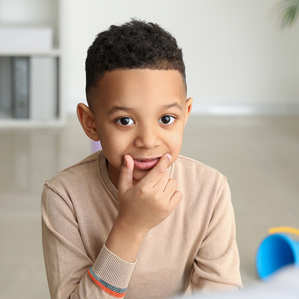 Child using hand at mouth to form sounds in speech-language therapy session, Adobe Stock.