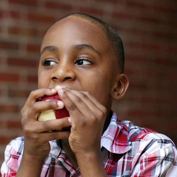 Adolescent boy eating red apple, by iStock.
