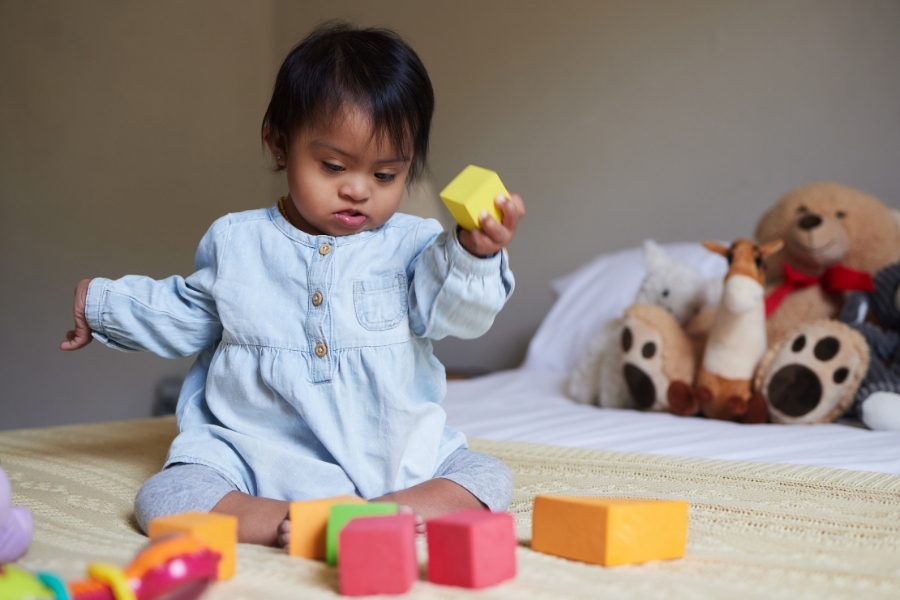 A baby sits on a bed, playing with blocks.