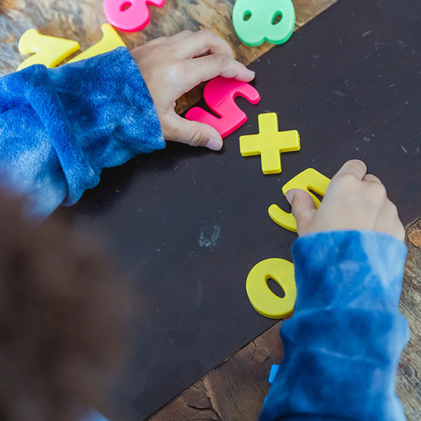 Child solving math problems with colorful toy numbers on a table, credit Keira Burton - Pexels.