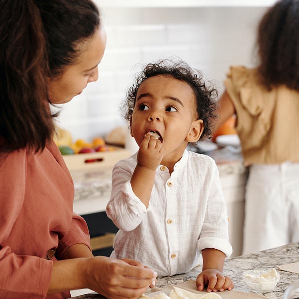 A woman helping a young child eat a snack at a kitchen island