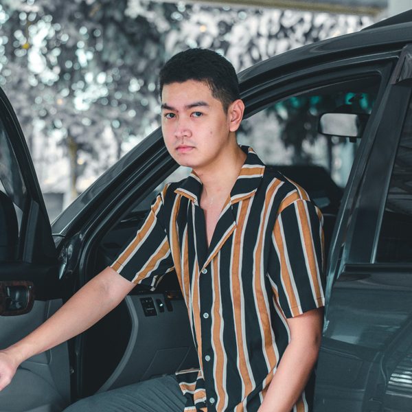 Young adult stands next to a car with the door open.