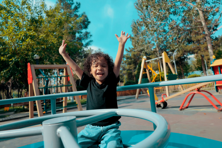 Child waving their arms while at a sunny playground.