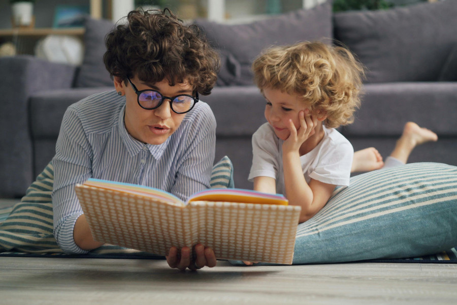 Caregiver reads book to child as they lie on the floor together.