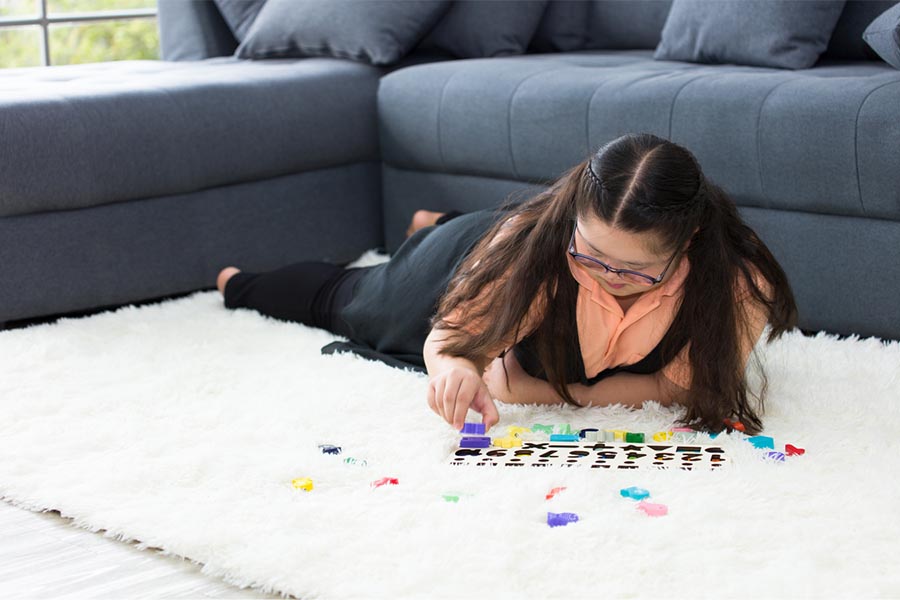 Teen laying belly down on floor playing puzzle, Canva.
