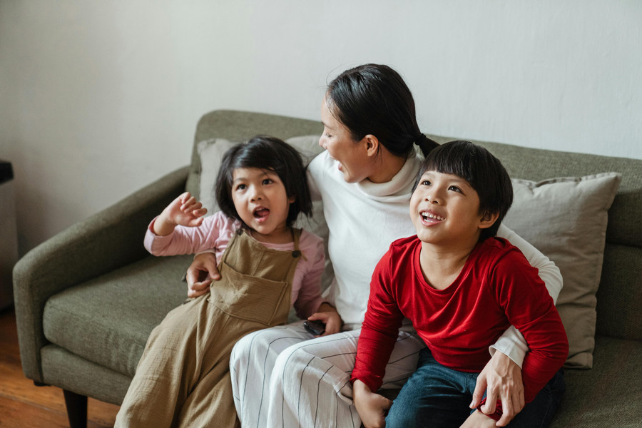 Caregiver sits on a couch with two smiling children.