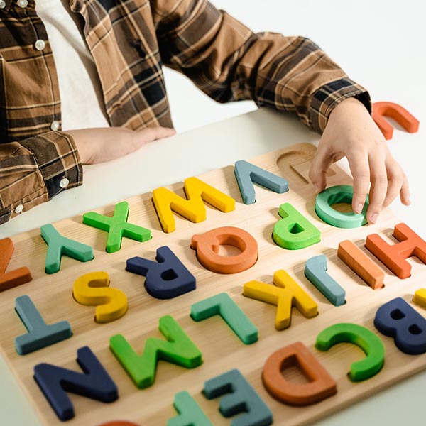 Child seated at a desk touching the letter O on a wooden alphabet board, credit Mart Production – Pexels.