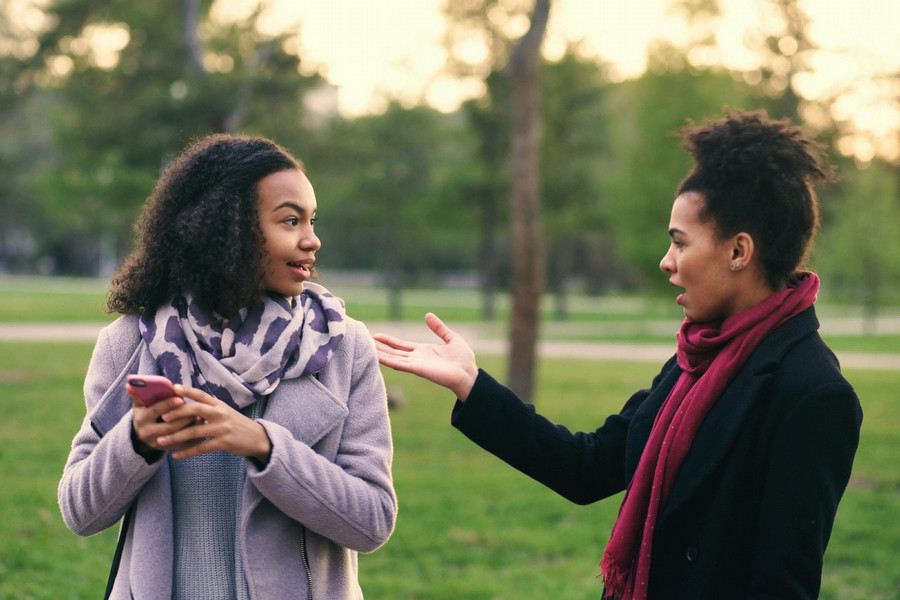 Two individuals talk outside in a sunlit park.