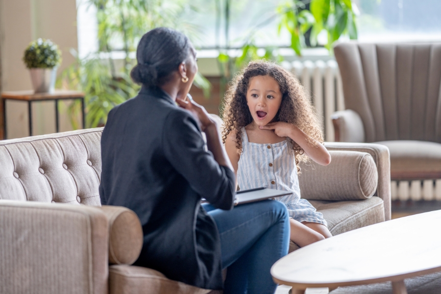 Seated child mimics finger placement on throat, same as the provider.
